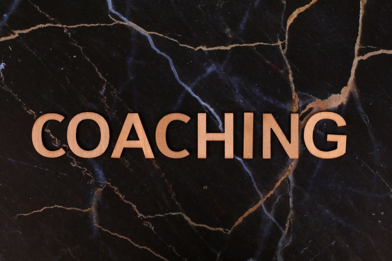 The Art of Drawing Readers In: Your attractive post title goes here Wooden letters spelling 'Coaching' on dark marble surface, emphasizing guidance and mentorship.